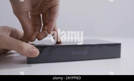 MOSKAU, RUSSLAND-NOVEMBER 2020: Nahaufnahme des Auspackens des iPhone. Aktion. Nahaufnahme des Mannes, der die Box vom neuen iPhone öffnet. Die Hand des Mannes löst den Film von der Box wi ab Stockfoto