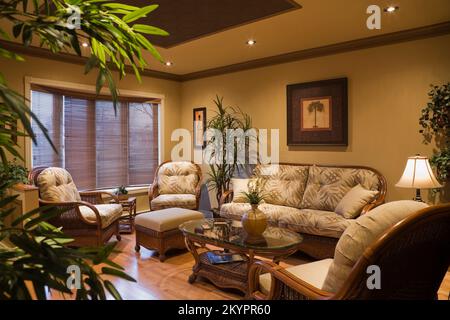 Korbsessel, Sofa und Couchtisch mit Glasplatte im Wohnzimmer in einem kleinen Bungalow-Haus, Quebec, Kanada. Dieses Bild ist Eigentum freigegeben. PR Stockfoto