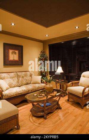 Korbsessel und Couchtisch mit Glasplatte im Wohnzimmer in einem kleinen Bungalow-Haus. Stockfoto