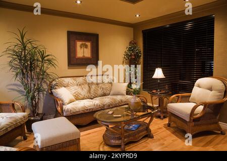 Korbsessel und Couchtisch mit Glasplatte im Wohnzimmer in einem kleinen Bungalow-Haus. Stockfoto