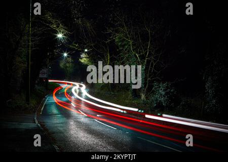 Symmetrische Lichtstrecken. Nachtaufnahme bei Regen mit langer Belichtung und markanten weißen und roten Rücklichtern auf der Straße, die unter Druck gehalten werden. Stockfoto