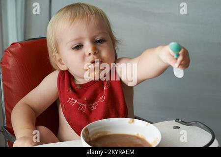 Wachsender Junge braucht sein Essen. Ein kleiner Junge, der in seinem Hochstuhl nach Herzenslust isst. Stockfoto