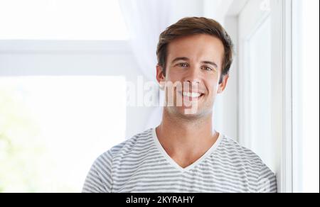 Ich bin froh, wieder zu Hause zu sein. Ein junger Mann in lässiger Kleidung, der vor der Kamera lächelt. Stockfoto