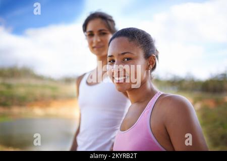 Joggen unter ländlicher Schönheit. Zwei junge Joggingweibchen lächeln fröhlich in die Kamera. Stockfoto