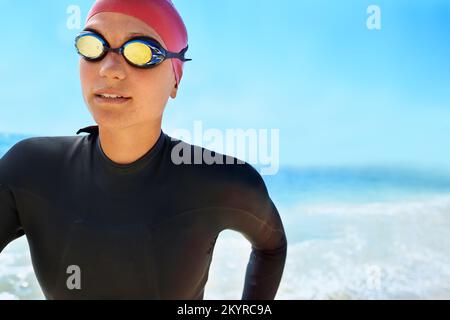 Training, um ein Lebensretter zu sein. Eine junge Frau, die im Winter am Strand in einem vollteiligen Neoprenanzug und Schwimmkleidung trainiert. Stockfoto