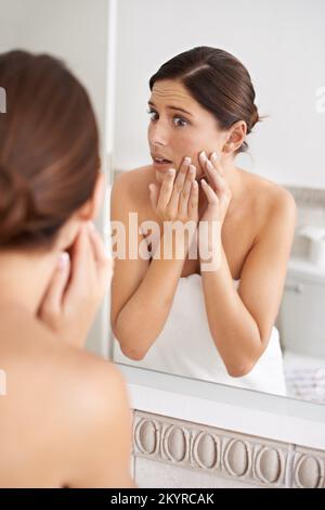 Das kann nicht wahr sein. Eine wunderschöne junge Frau, die ihren Pickel schockiert ansieht. Stockfoto