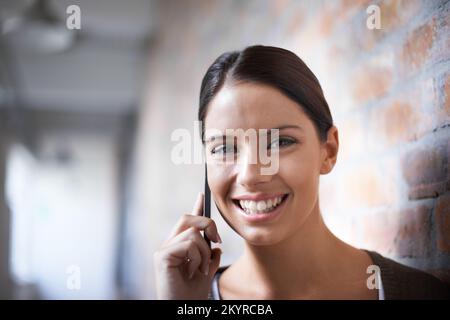 Ich bin immer nur einen Anruf entfernt. Lächelnde junge Frau mit ihrem Smartphone. Stockfoto