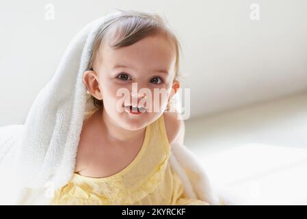 Sie lacht immer. Ein süßes kleines Mädchen, das auf dem Boden sitzt und mit der Decke spielt. Stockfoto