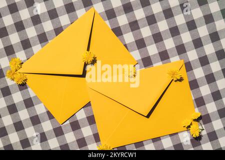 Wunderschöne kleine gelbe Kamillenblüten auf zwei Briefumschlägen in Gelb, leeres Papier, Platz für Text, Frühling, Grußkarte für Urlaub. Blumenlieferung. Zarte gelbe Blumen Stockfoto