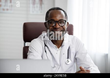 Ein afroamerikanischer Arzt begrüßt die Online-Patientenberatung auf dem Laptop. Ein Büro, das telemedizinische Dienste erbringt. Online-Medizin und Stockfoto