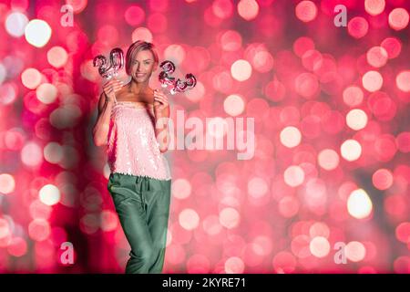 Frohes Neujahr 2023 in trendigen kreativen Designs in Farbe. Frau mit goldenen Ballons in Form von Zahlen auf glänzenden Bokeh-Lichtern auf festlichem Hintergrund. Toning in Viva Magenta. Hochwertiges Foto Stockfoto