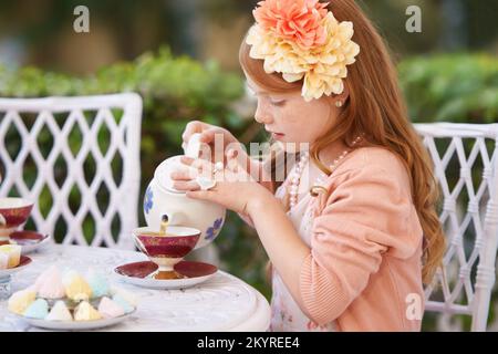 Eine Teeparty veranstalten. Ein süßes kleines Mädchen, das draußen eine Teeparty veranstaltet. Stockfoto