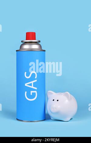 Gaskartuschenflasche mit Sparschwein auf blauem Hintergrund. Konzept der Gaseinsparung Stockfoto