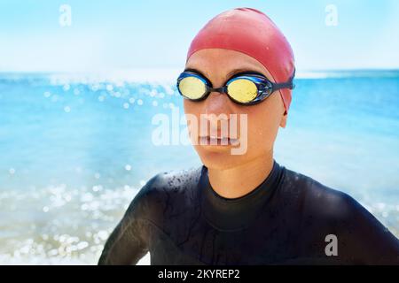 Training, um ein Lebensretter zu sein. Eine junge Frau, die im Winter am Strand in einem vollteiligen Neoprenanzug und Schwimmkleidung trainiert. Stockfoto