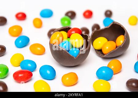 Gebrochene Schokolade osterei mit bunten Süßigkeiten Dekorationen auf weißem Hintergrund mit bunten Süßigkeiten. Süße Ostertradition. Stockfoto