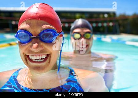 Bereit zum Schwimmen. Ein Mann und eine Frau stehen in einem Pool und tragen Schutzbrillen und Badekappen. Stockfoto