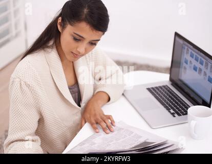 Sie interessiert sich für die Nachrichten um sie herum. Eine junge Frau, die an ihrem Laptop sitzt und Zeitung liest. Stockfoto