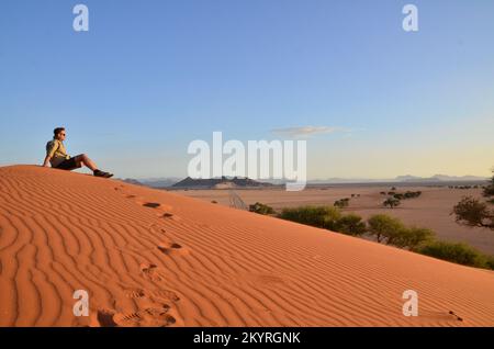 Mann sitzt auf der Düne in der Trockenpfanne des Sossusvlei Namib Naukluft Nationalparks Stockfoto