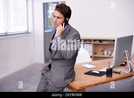 Lösen von Geschäftsproblemen per Mobiltelefon. Ein junger Geschäftsmann, der in seinem Büro ein wichtiges Gespräch führt. Stockfoto