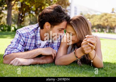 Romantik ist für sie ganz natürlich. Ein glückliches junges Paar, das im Park auf dem Gras liegt. Stockfoto