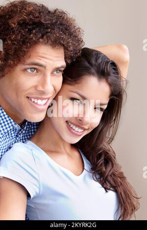 Mein Mann. Studiofoto eines gutaussehenden jungen ethnischen Mannes, der seine Freundin von hinten umarmt und wegschaut. Stockfoto