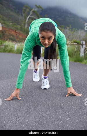 Bereit, diese Straße zu ihrer eigenen zu machen... Eine junge Frau, die auf der Straße hockend, um zu laufen. Stockfoto