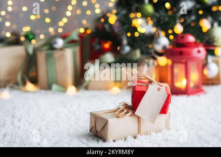 Weihnachtsgeschenk mit Anhängern zum Schreiben. Im Hintergrund befinden sich ein Weihnachtsbaum und Geschenke mit Lichtern. Neujahrshintergrund. Stockfoto