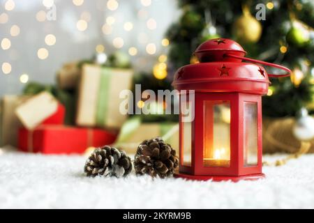 Weihnachtskerzen und Geschenk mit Anhängern zum Schreiben. Im Hintergrund befinden sich ein Weihnachtsbaum und Geschenke mit Lichtern. Neujahrshintergrund. Stockfoto