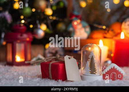 Weihnachtsgeschenk mit Anhängern zum Schreiben. Im Hintergrund befinden sich ein Weihnachtsbaum und Geschenke mit Lichtern. Neujahrshintergrund. Stockfoto