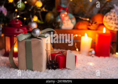 Weihnachtsgeschenk mit Anhängern zum Schreiben. Im Hintergrund befinden sich ein Weihnachtsbaum und Geschenke mit Lichtern. Neujahrshintergrund. Stockfoto