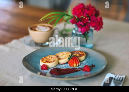 Hüttenkäse-Pfannkuchen oder Syrniki mit Himbeermarmelade auf einem grünen Teller Stockfoto
