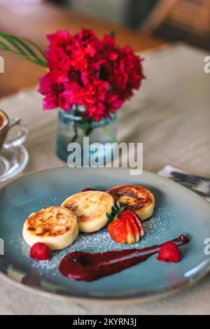 Hüttenkäse-Pfannkuchen oder Syrniki mit Himbeermarmelade auf einem grünen Teller Stockfoto