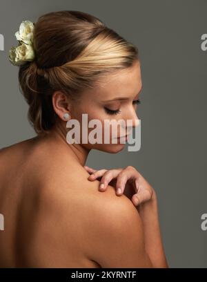 Anmut und zeitlose Eleganz. Studioaufnahme von einer attraktiven jungen Frau mit einer Blume im Haar. Stockfoto