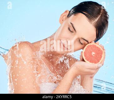 Schönheit, Spritzer und Wasser mit einer Frau, die Obst für Gesundheit, Hautpflege und Wellness auf blauem Studiohintergrund hält. Sauber, Dusche und Kosmetik mit einem Stockfoto