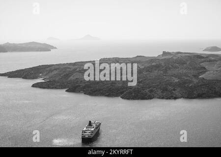 Santorin, Griechenland - 16. September 2022 : Blick auf ein Kreuzfahrtschiff neben dem berühmten Vulkan Santorin in Schwarz-Weiß Stockfoto