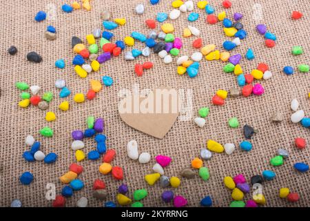 Herz aus Papier inmitten der bunten Steinchen auf Leinwand Boden Stockfoto