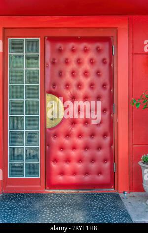 Hellrote gepolsterte Tür am Eingang eines Restaurants in Austin Texas. Außenseite einer Bar mit gepolsterter Tür, dickem Seitenlicht aus Milchglas und Vib Stockfoto