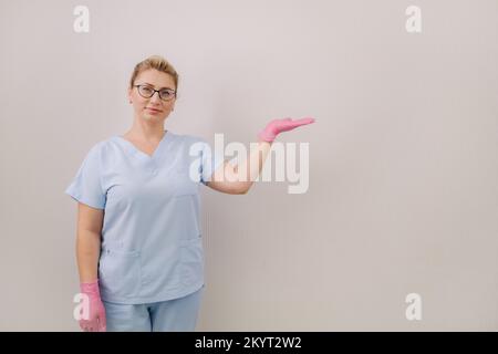 Eine Ärztin in rosa Handschuhen zeigt ihre Hand auf einem hellen Hintergrund zur Seite Stockfoto