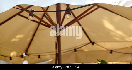 Restaurant Terrasse Sonnenschirm mit Glühbirnen. Ausrüstung für Café Abendbeleuchtung. Verschwommenes Bild, selektiver Fokus Stockfoto