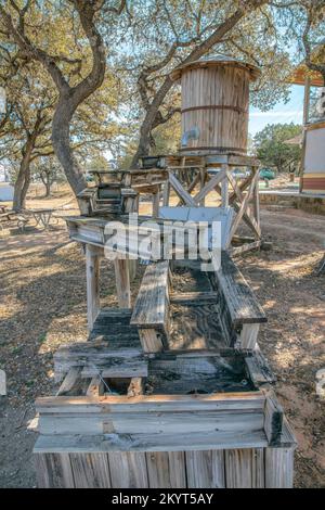 Kleiner Wasserspeicher aus Vinatgeholz mit Metallrohr und Holzwasserkanal. Altes Wasserfass vor einer malerischen Landschaft des Austin-Sees, Bäume und Blau Stockfoto