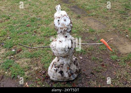 Ein trauriger Schneemann schmilzt. Er hält eine Karotte in den Händen. Zu wenig Schnee im Winter. Klimawandel. Globale Erwärmung. Auf Wiedersehen Winter, hallo Frühling! Stockfoto
