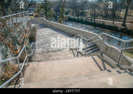 Treppen im Freien mit Blick auf den Kanal und Park am San Antonio River Walk Texas. Sonnige Tageslandschaft mit Betontreppe entlang des Flusses an einem Popul Stockfoto