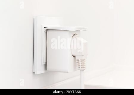 Weiße europäische Steckdose mit intelligentem Stecker im modernen, hellen Badezimmer mit weiß gefliesten Wänden Stockfoto