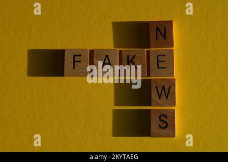 Fake News, Wörter in hölzernen Buchstaben in Kreuzworträtselform isoliert auf gelbem Hintergrund Stockfoto