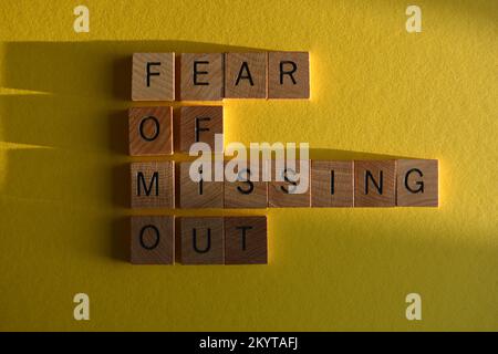 FOMO, Internet-Slang oder Text sprechen aus Angst, dass sie in hölzernen Buchstaben auf gelbem Hintergrund mit Schatten fehlen Stockfoto