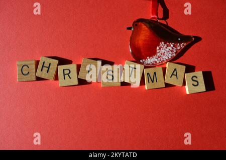 Robin-Dekoration und Weihnachten in hölzernen Buchstaben isoliert auf rotem Hintergrund mit Kopierbereich Stockfoto
