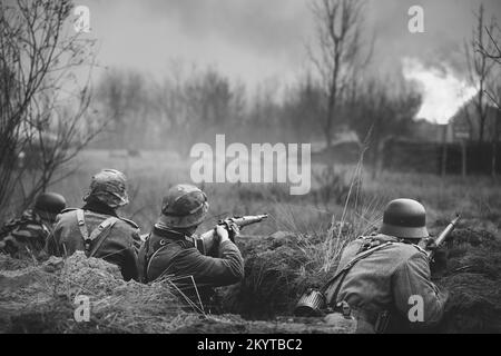 Nachbemaler bewaffneter Gewehre und gekleidet als deutsche Wehrmacht-Infanterie-Soldaten aus dem Zweiten Weltkrieg, die in Trench defensiv kämpfen. Verteidigungsposition. Gebäude Stockfoto