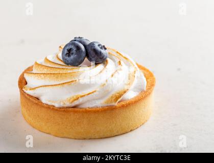 Köstlicher Zitronenkuchen mit süßem Baiser und mit Blaubeeren dekoriert, heller Hintergrund Stockfoto