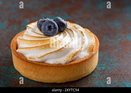 Köstlicher Zitronenkuchen mit Baiser und mit Blaubeeren dekoriert, dunkler Hintergrund Stockfoto