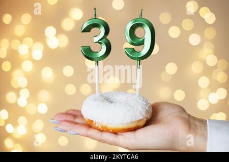 Eine Frau, die einen Kuchen mit den Kerzen Nummer 39 auf festlichem, verschwommenem Bokeh-Hintergrund hält. Stockfoto